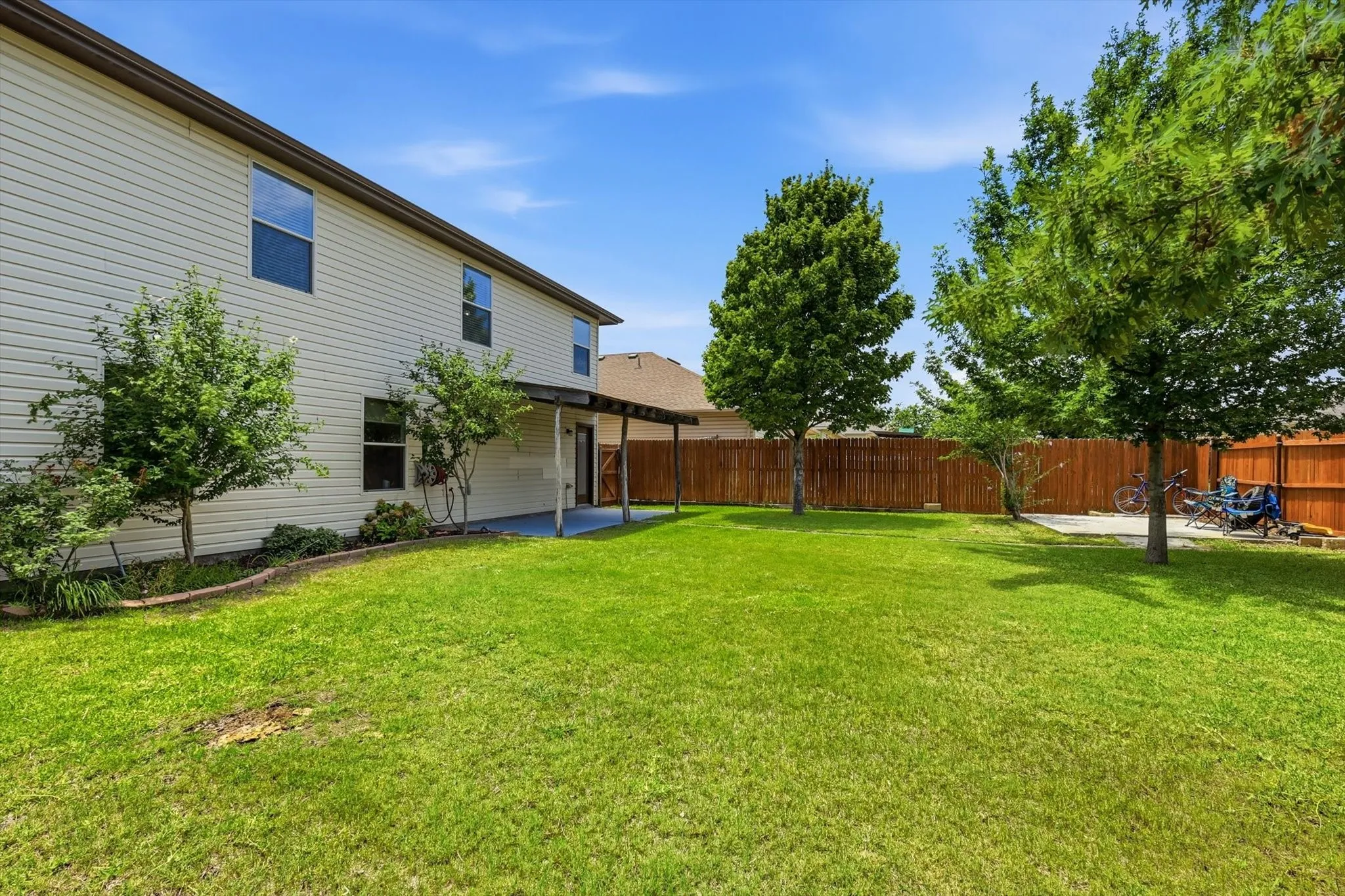 Expansive backyard featuring a manicured lawn with mature shade trees and wooden privacy fencing