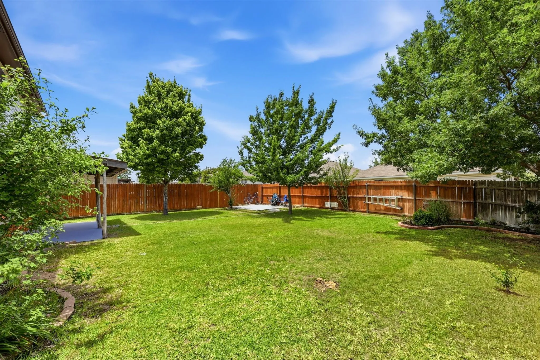 Expansive backyard featuring a manicured lawn, mature shade trees, and wood-finish fencing