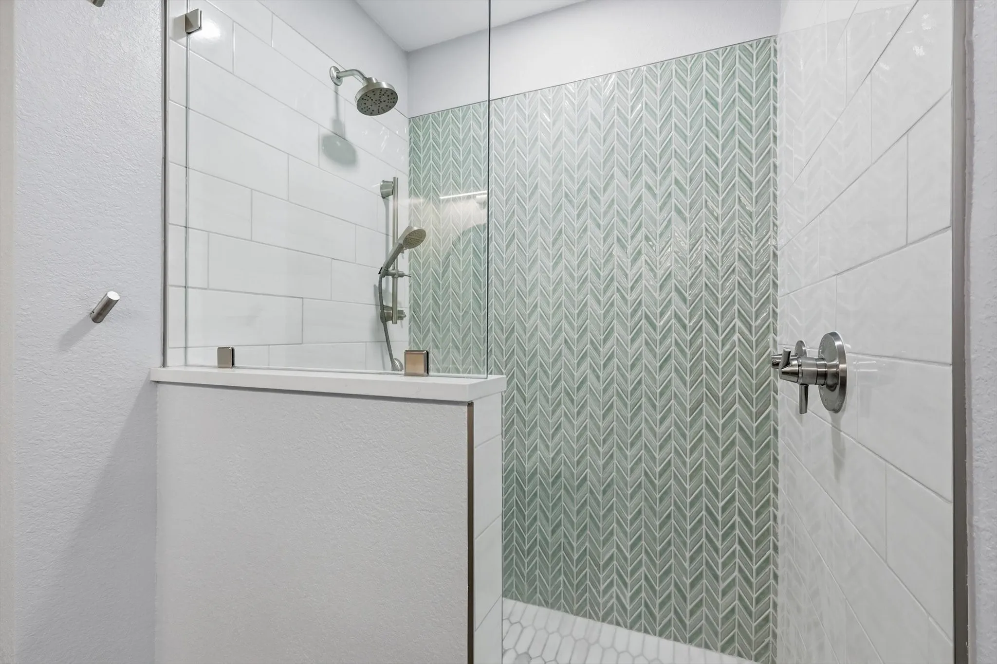 Glass-enclosed shower with a rainfall showerhead, handheld sprayer, and herringbone accent tile
