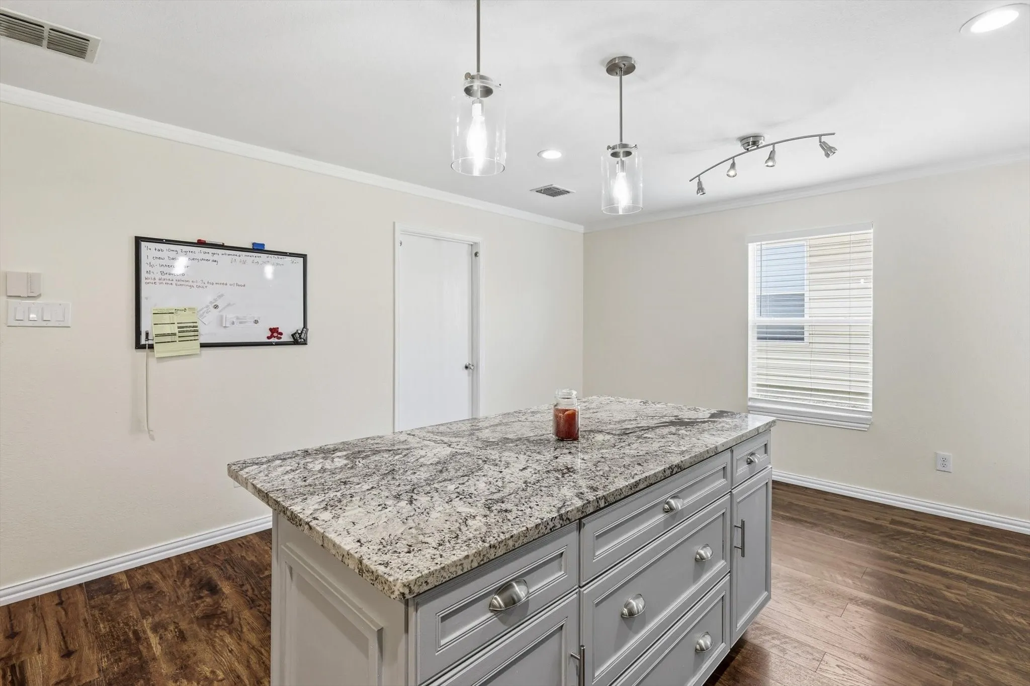 Modern kitchen island featuring a granite-look countertop with waterfall edge, gray cabinetry with multiple drawers, and stainless steel hardware