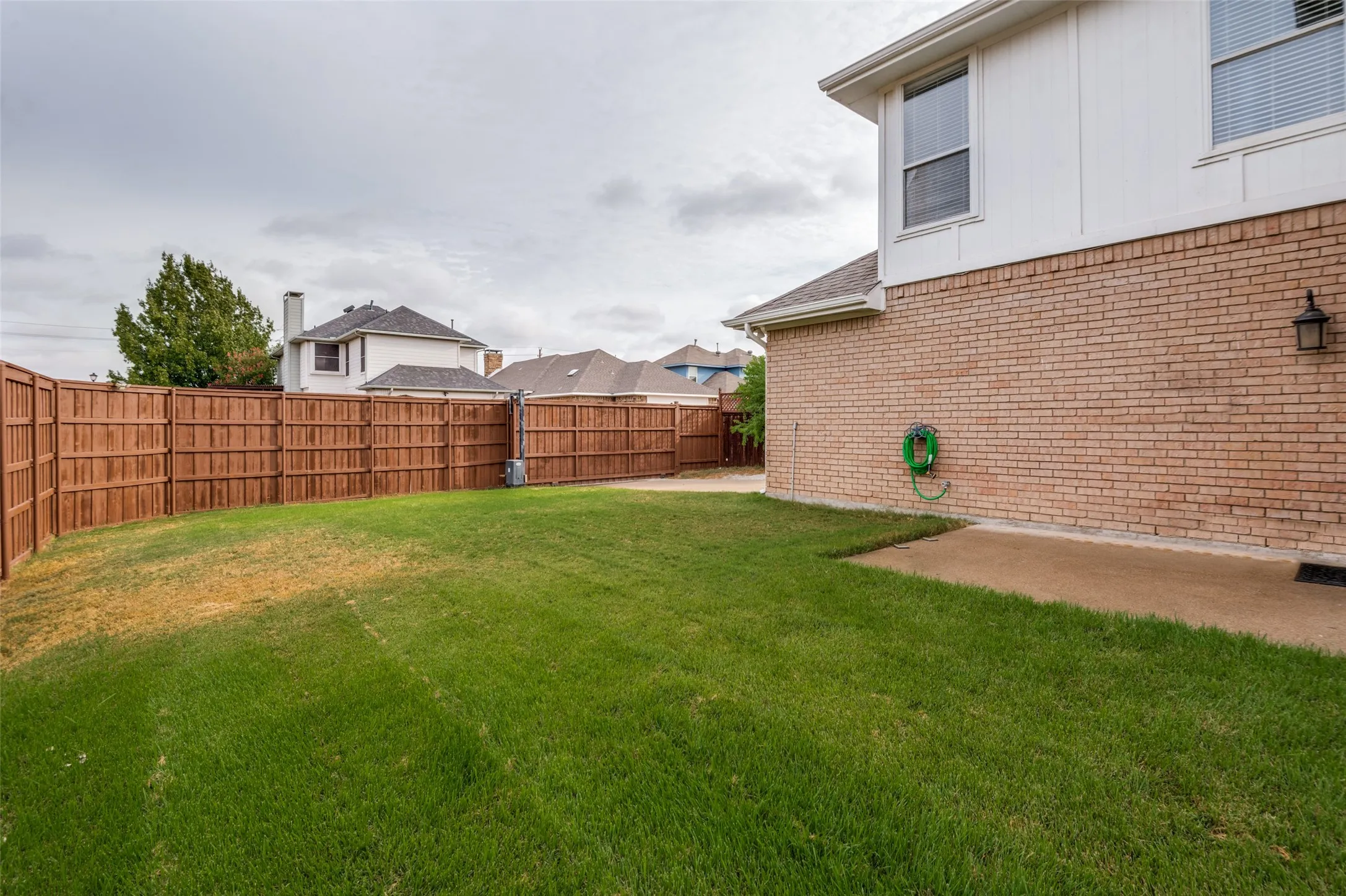 Expansive backyard with a manicured lawn, full privacy fencing, a concrete patio, and a brick and siding exterior