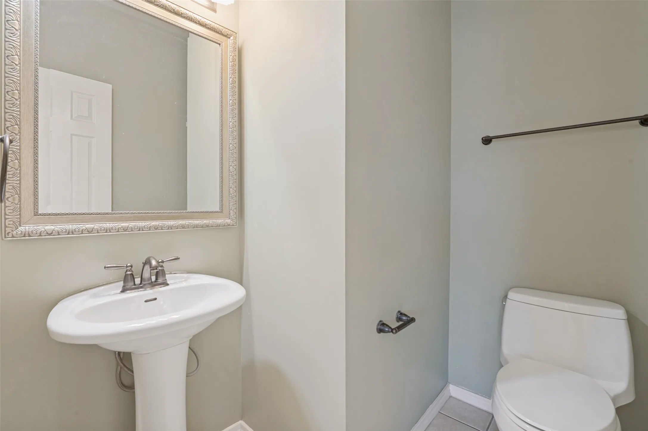 Pedestal sink with brushed nickel faucet, ornate framed mirror, and tile flooring
