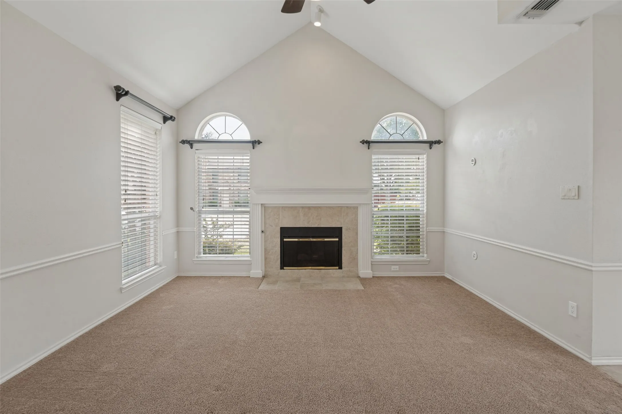 Vaulted ceiling, arched top window, fireplace with stone surround, chair rail molding, and neutral carpeting