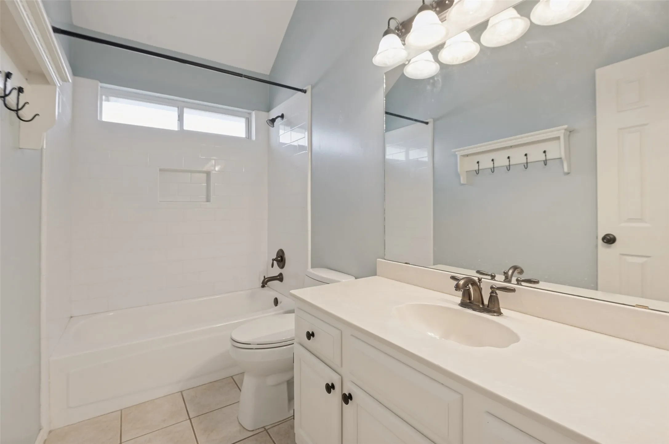 White subway tile shower surround with an integrated niche, bronze-finish fixtures, a vanity with an integrated sink, and an overhead mirror with a five-light fixture