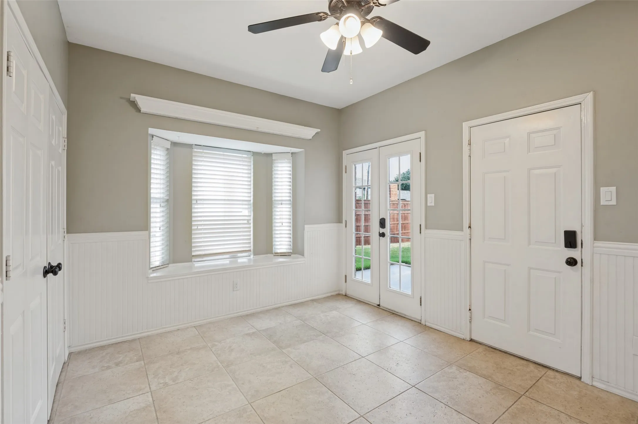Bright sunroom featuring expansive windows with plantation shutters, ceramic tile flooring, ceiling fan with integrated lighting, and French doors opening to the backyard