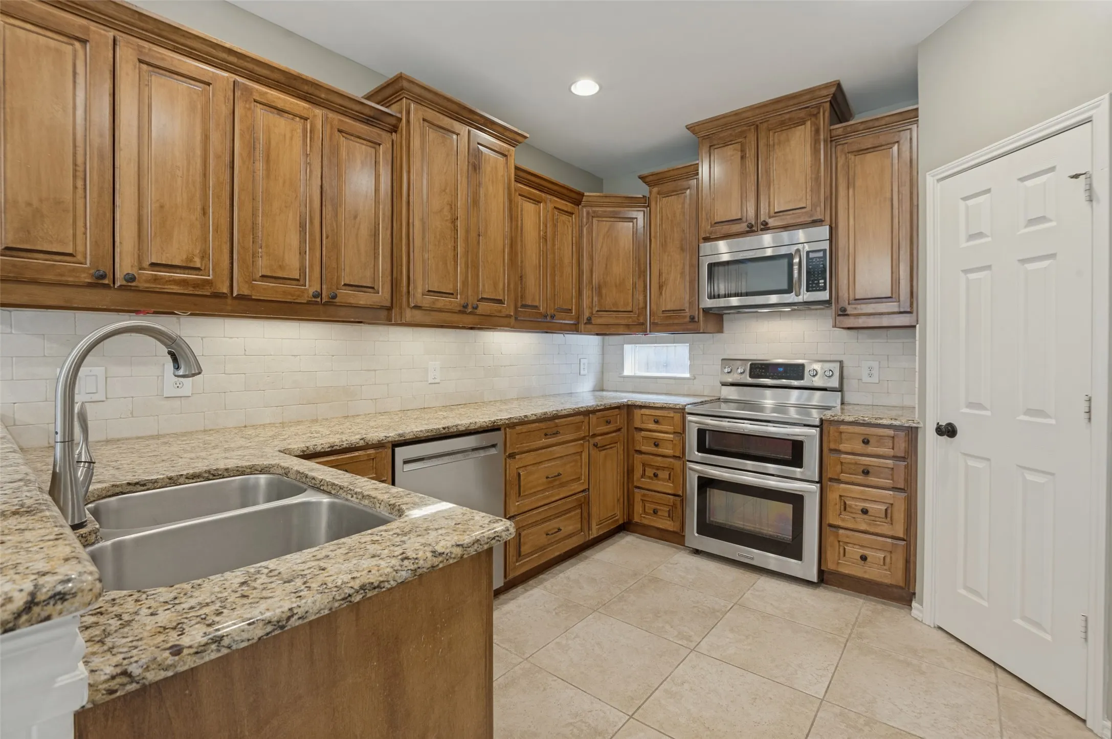 U-shaped kitchen with wood cabinetry, light-toned granite countertops, and a subway tile backsplash