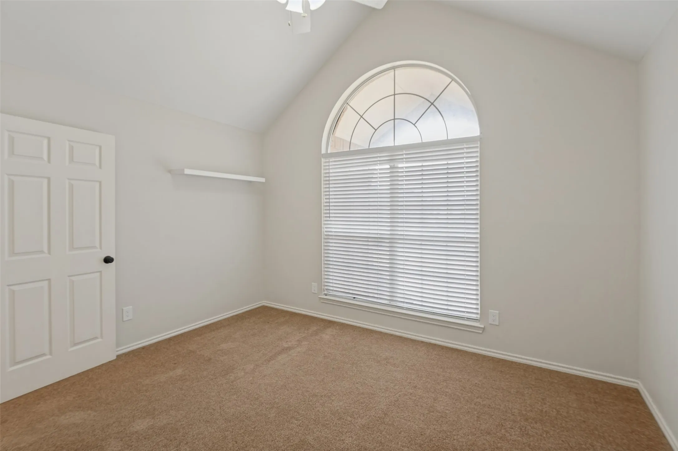 Vaulted ceiling with a ceiling fan, arched window with divided lites, horizontal blinds, carpeted flooring, and a paneled door