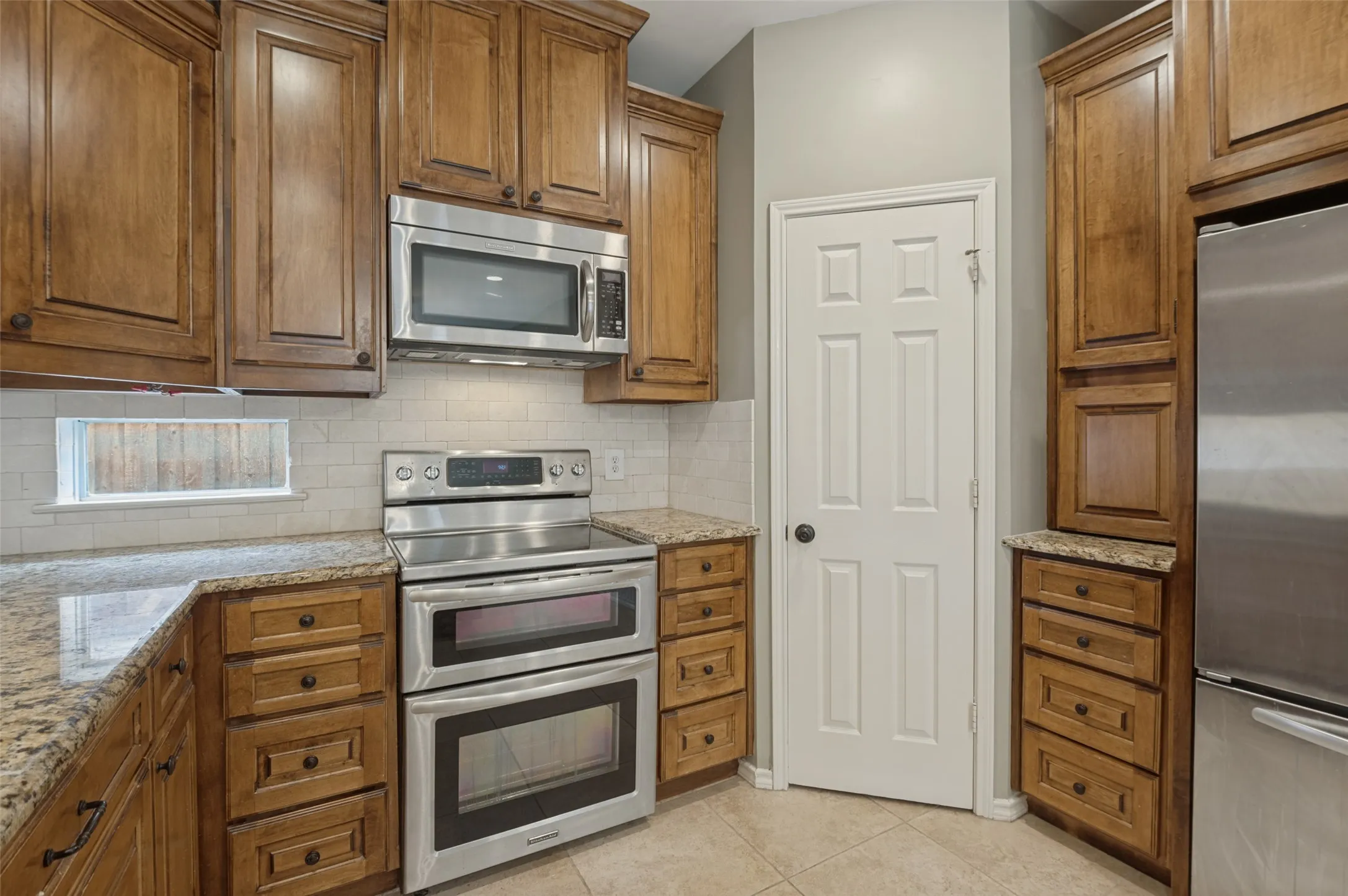 Kitchen featuring wood cabinetry, stainless steel appliances, granite countertops, and a tiled backsplash