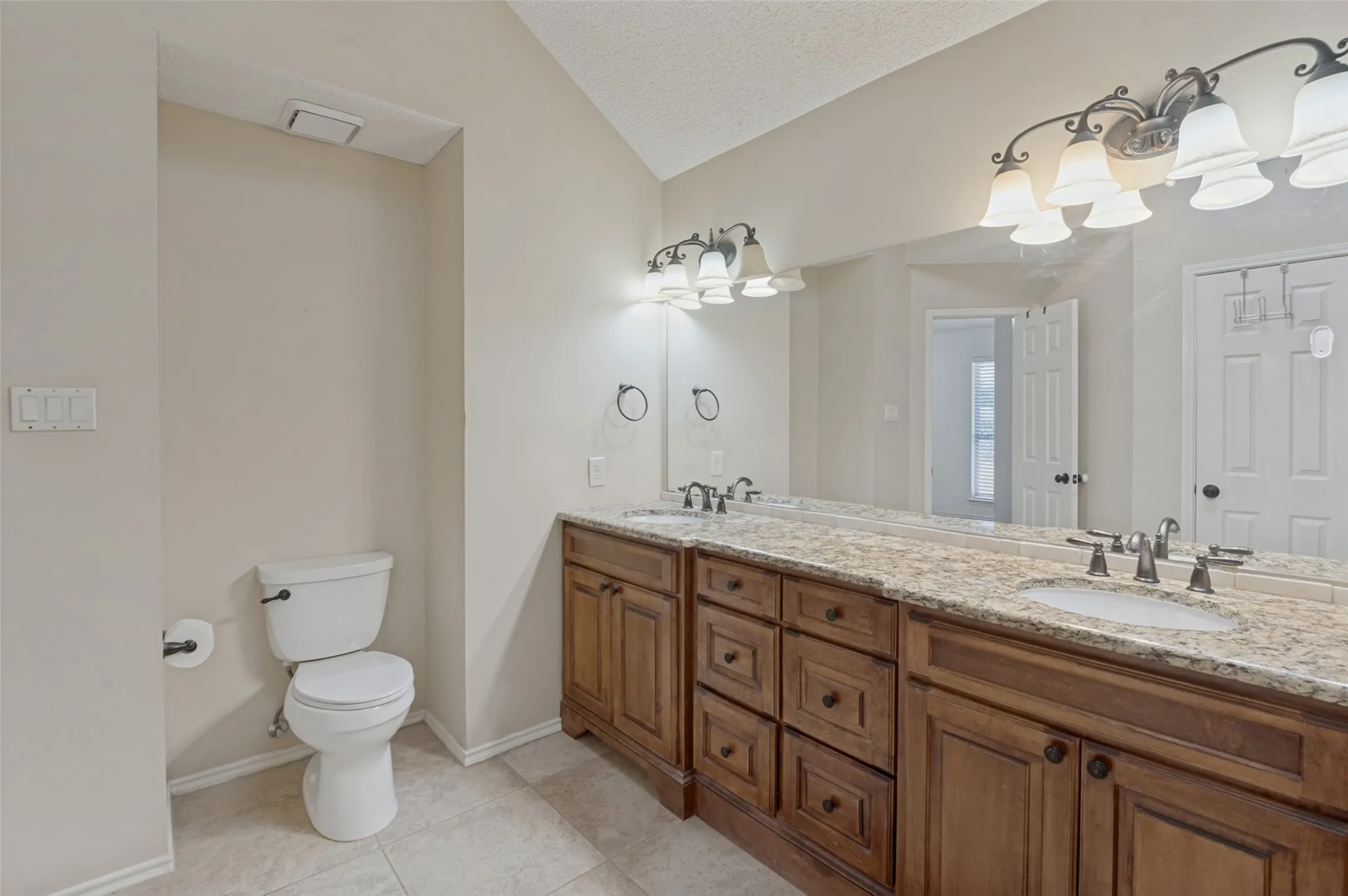 Vaulted ceiling bathroom featuring a dual vanity with wood cabinetry, light-toned countertops, and tile flooring