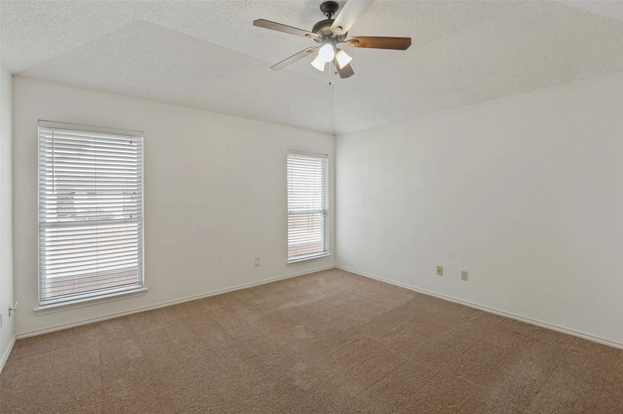 Neutral wall paint, textured ceiling, two windows with blinds, ceiling fan with light, and carpeted flooring