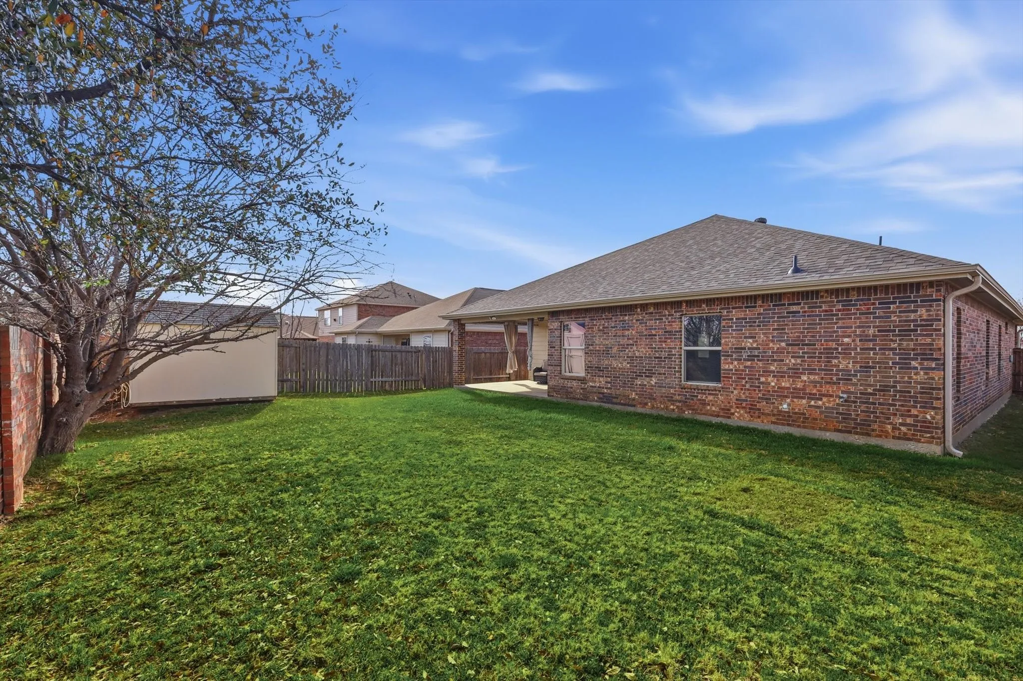 Expansive backyard featuring a manicured lawn, brick exterior, covered patio, and wood privacy fencing