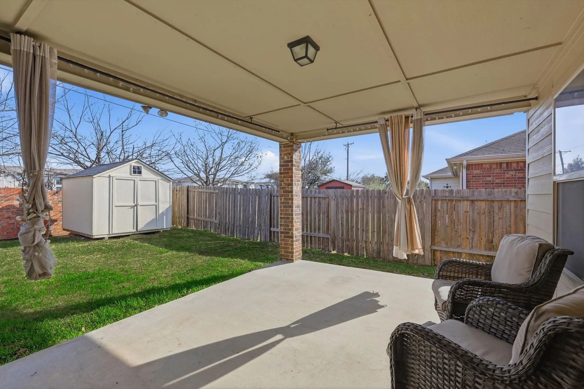 Covered patio with concrete flooring, wood privacy fencing, and a detached storage shed