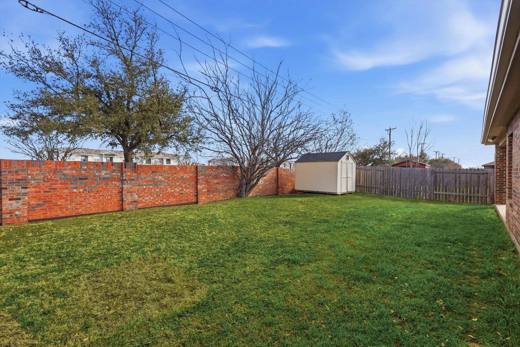 Expansive grass lawn with a brick perimeter wall, wood fence, and a detached storage shed