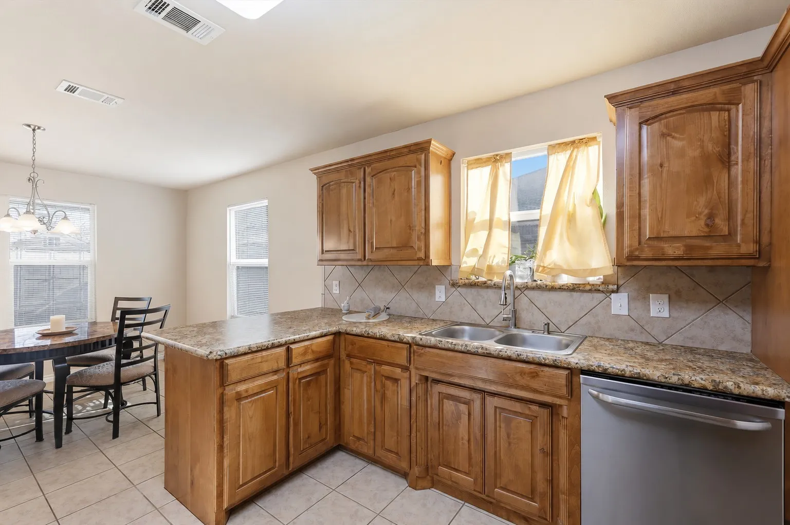 Kitchen featuring wood cabinetry, stone-finish countertops, a tile backsplash, and a stainless steel dishwasher