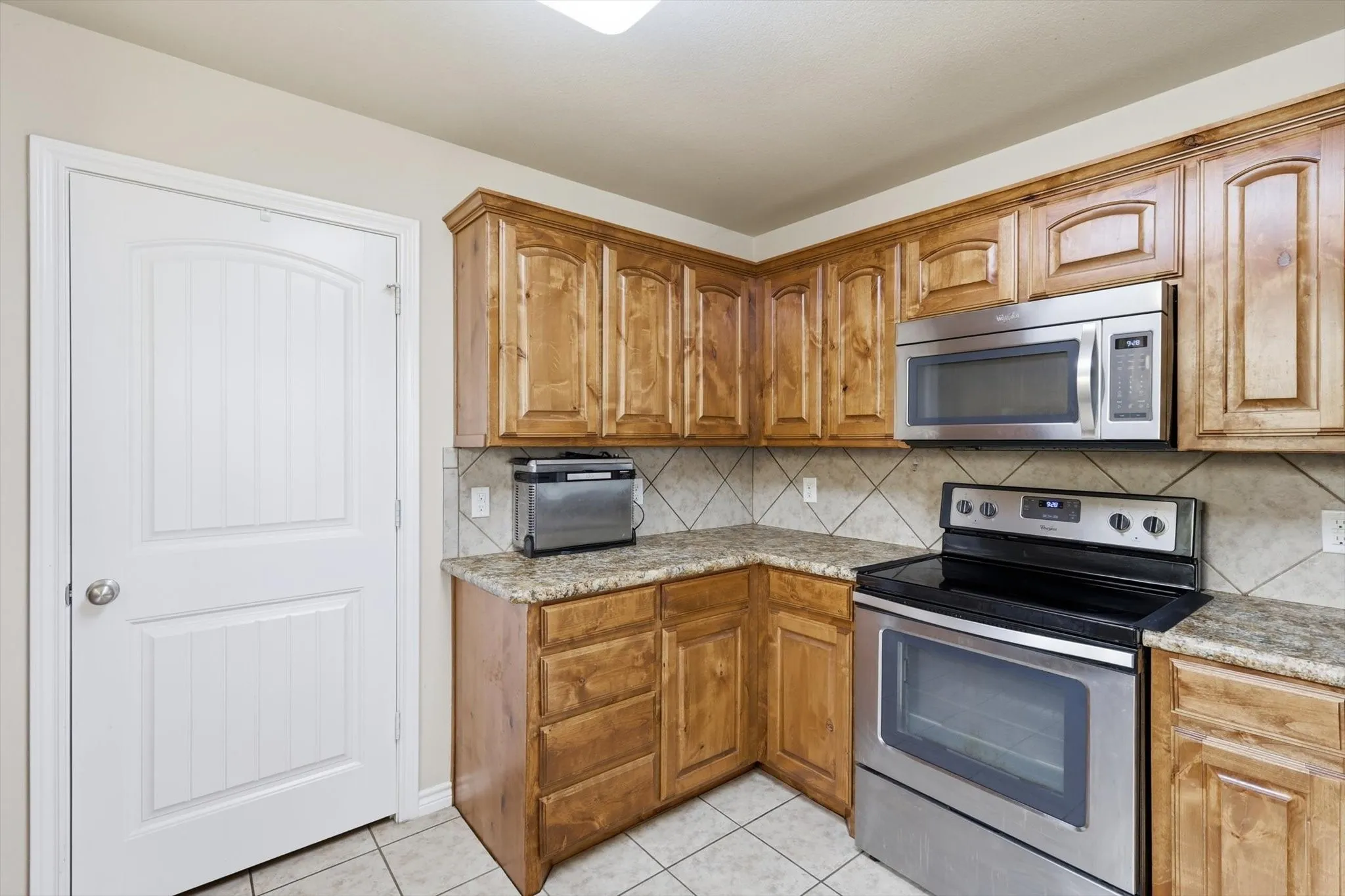 Wood-finish cabinetry, tile flooring, stainless steel range, stainless steel microwave, and a tile backsplash