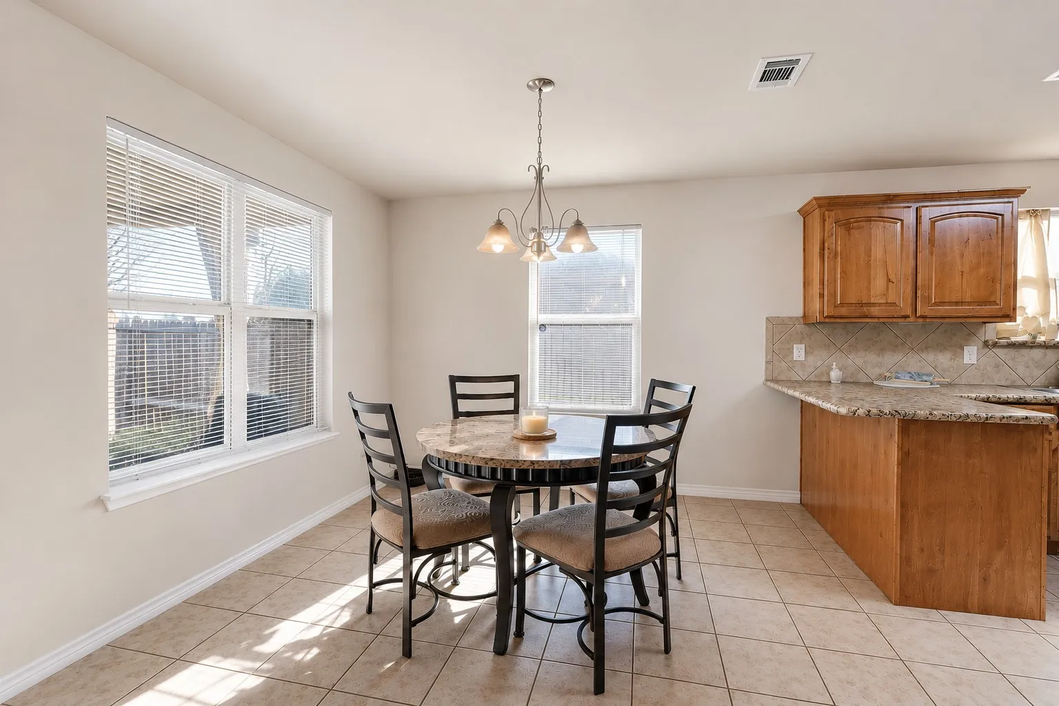 Tile flooring, two windows with blinds, wood cabinetry, stone-finish countertops, and a tile backsplash