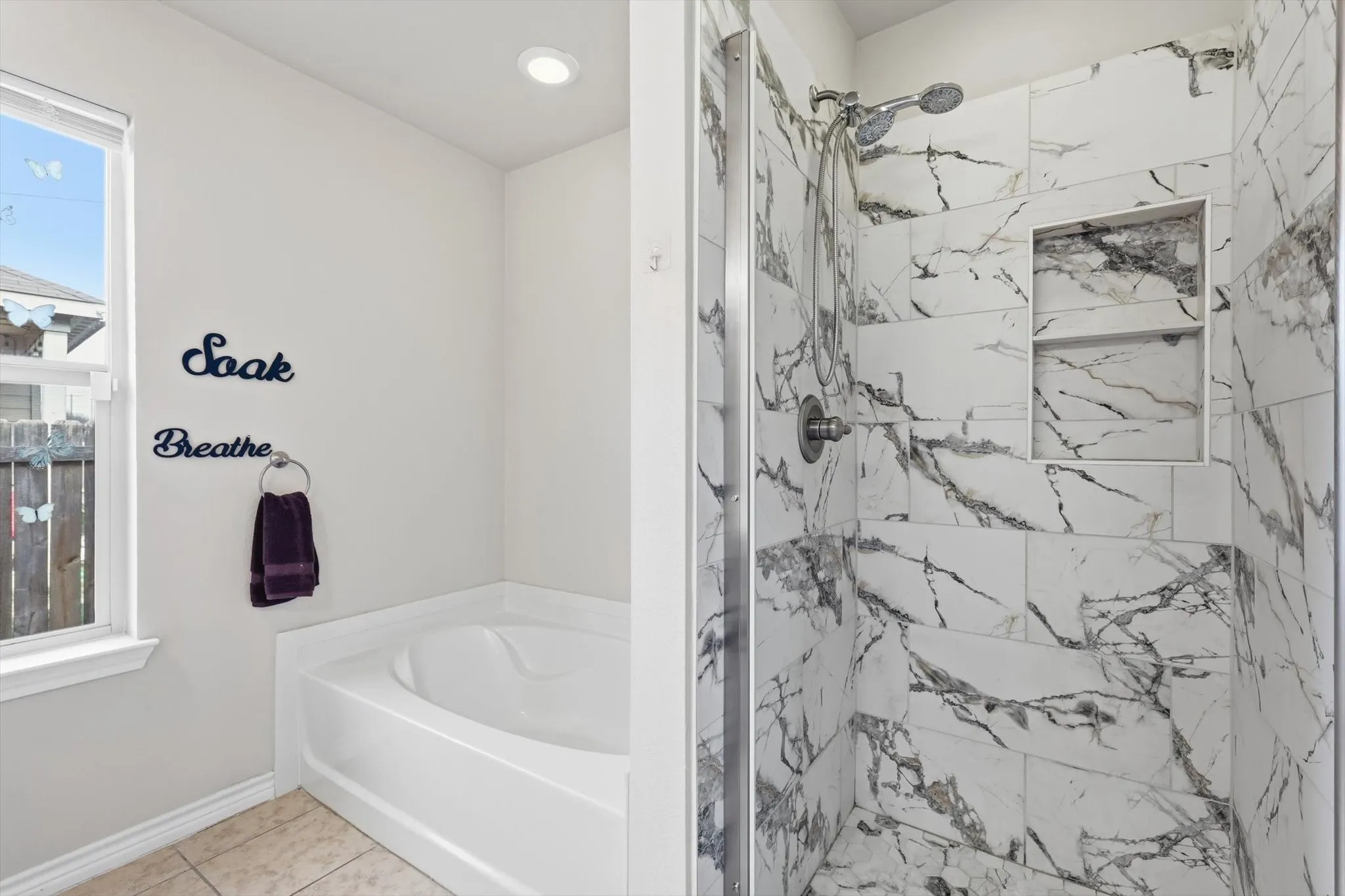 White soaking tub with window, recessed lighting, and a walk-in shower with large format tile and built-in shelving