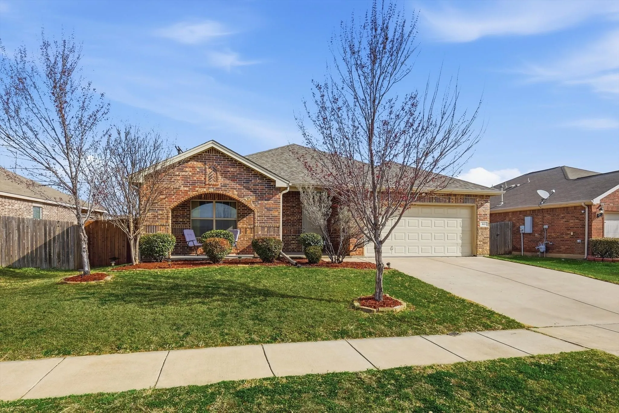 Brick exterior with an arched entryway, attached garage, concrete driveway, and a fenced side yard
