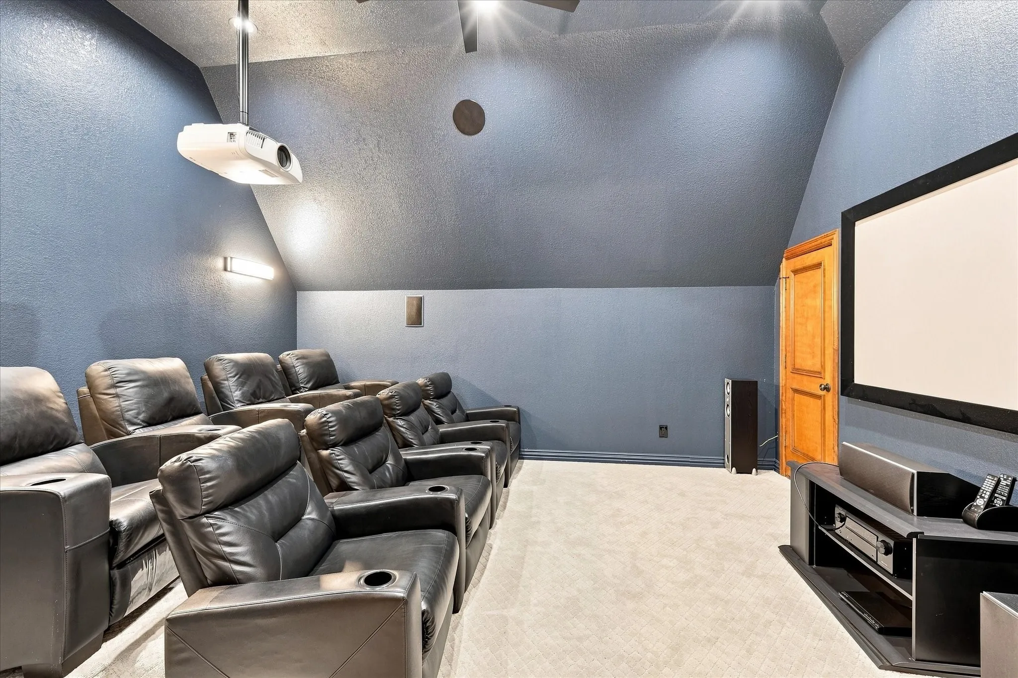 Integrated ceiling-mounted projector, wall-mounted screen, accent lighting, recessed audio speakers, and light-toned carpet flooring