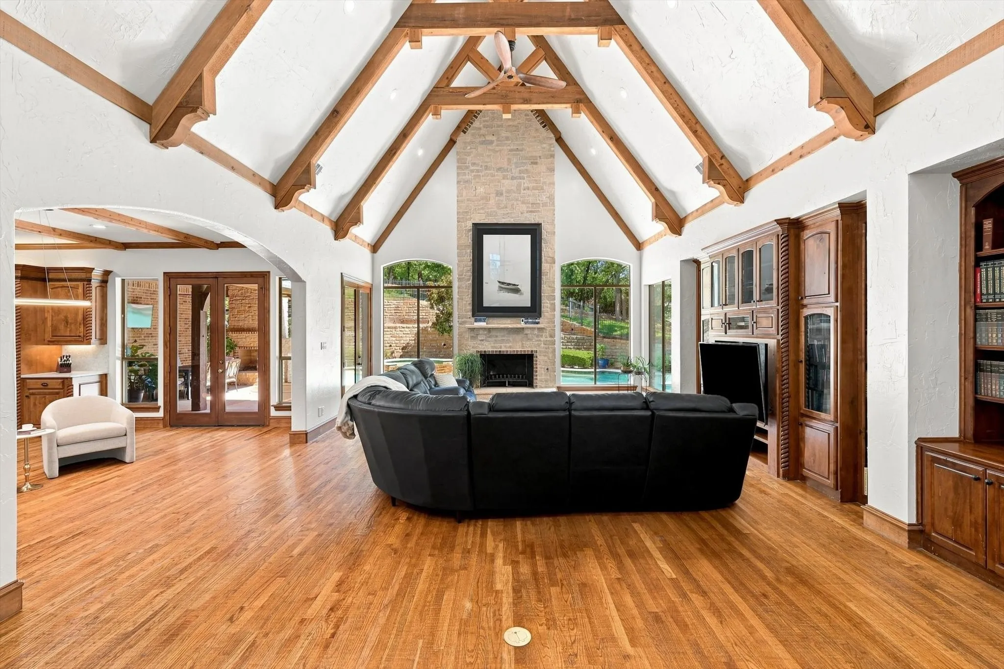 Vaulted ceiling with exposed wood beams, stone-faced fireplace, hardwood flooring, built-in entertainment center, and integrated shelving