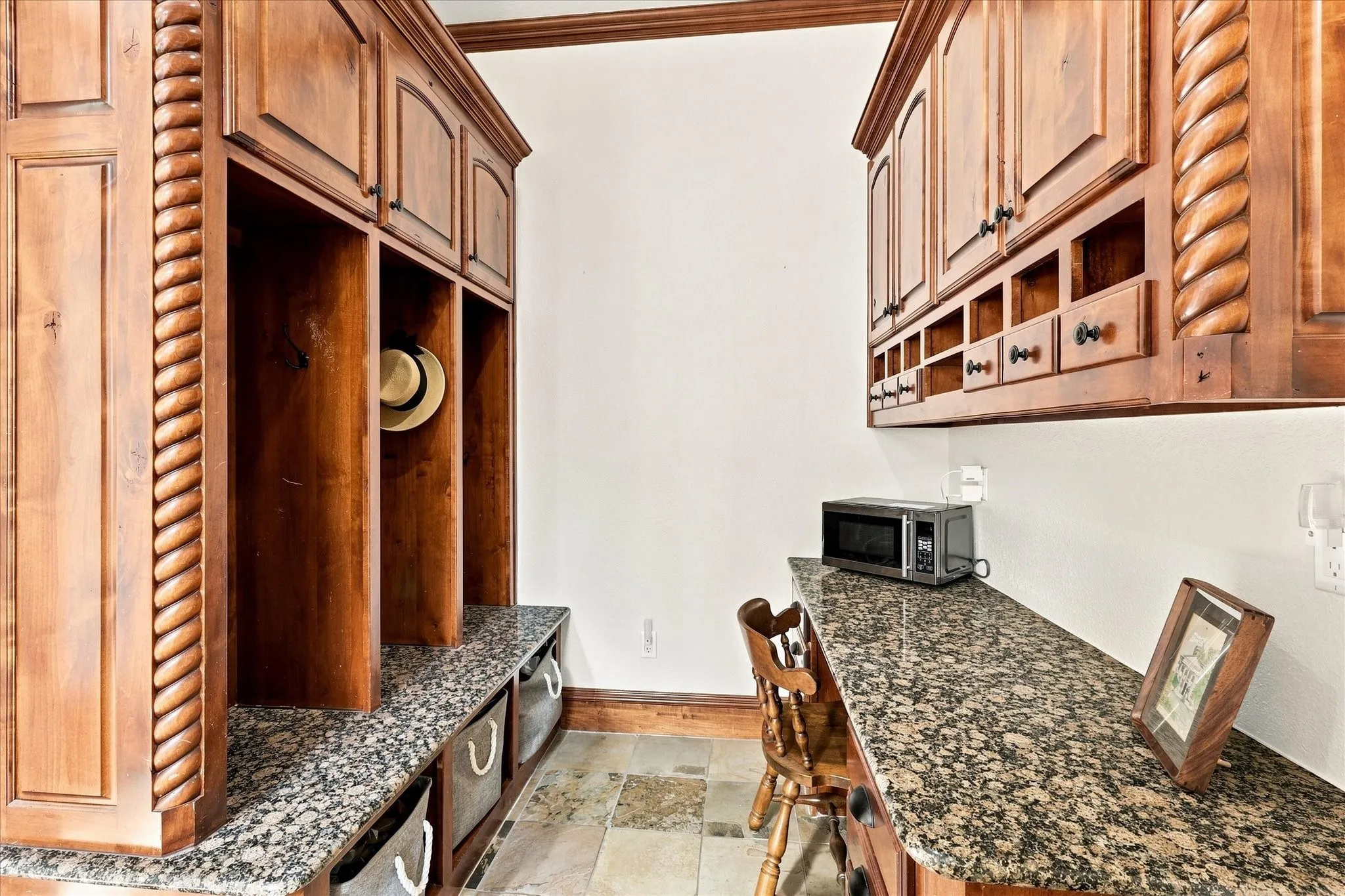 Built-in cabinetry with decorative rope molding, granite countertops, stone tile flooring, and integrated storage cubbies