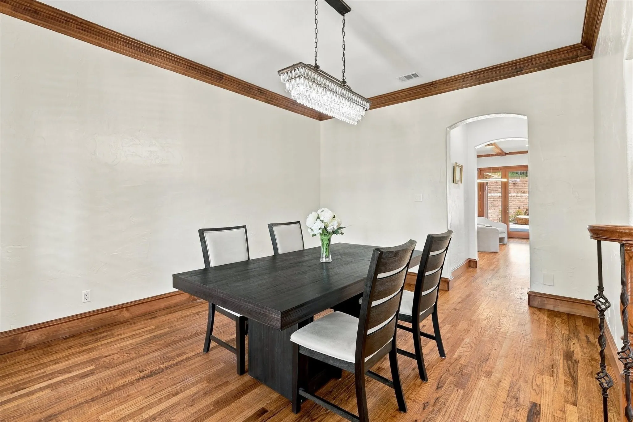 Hardwood flooring, decorative wood crown molding, arched entryway, and a crystal chandelier