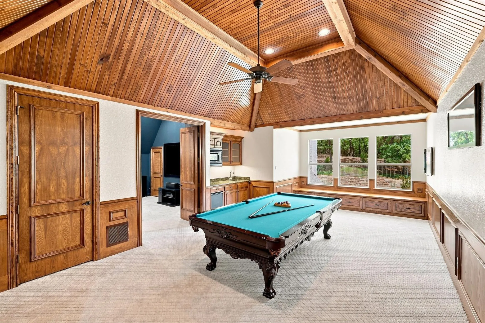 Vaulted wood-paneled ceiling, integrated wet bar with cabinetry, built-in window seating with storage, and a series of three windows