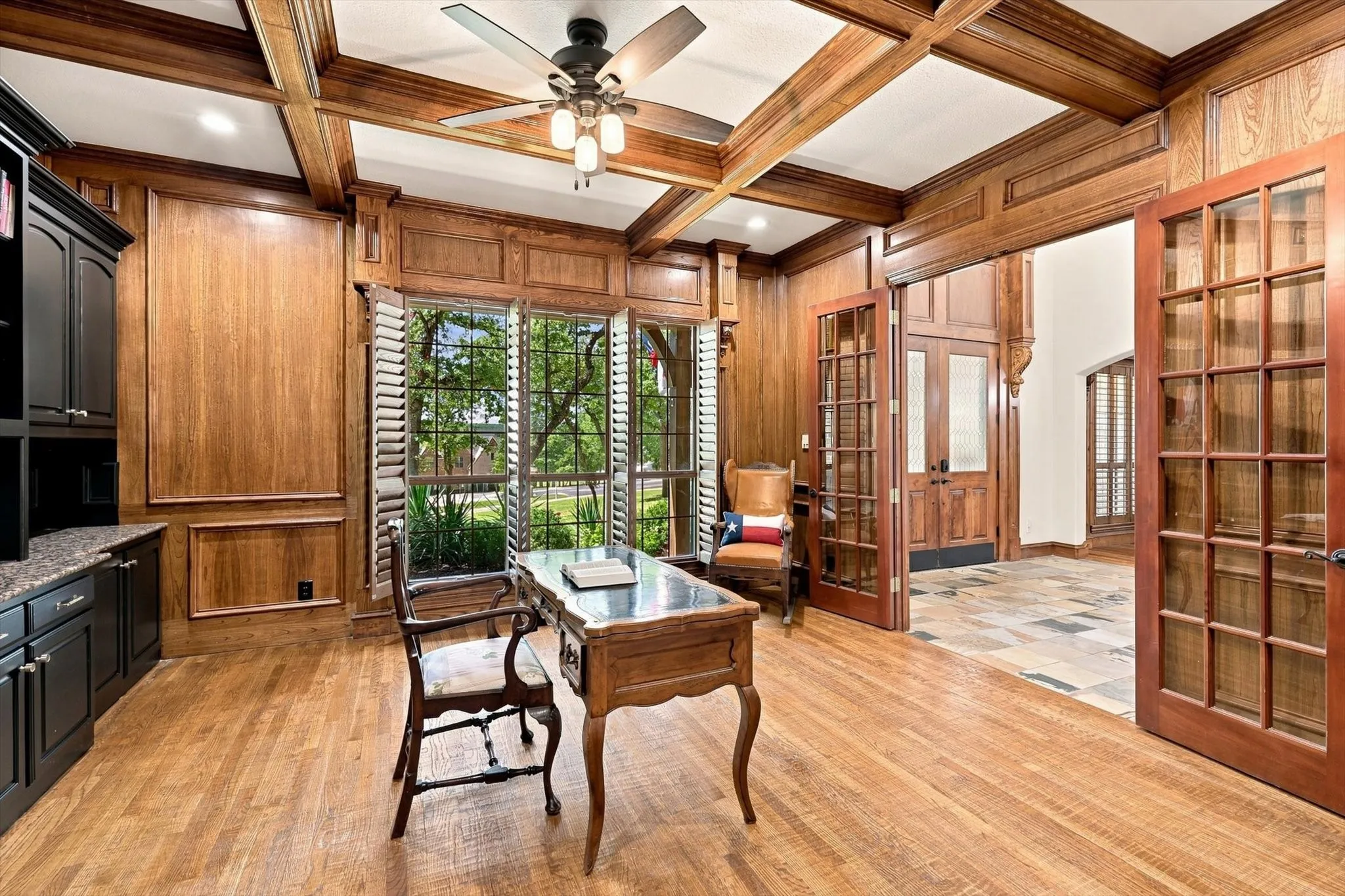 Wood-paneled room featuring a coffered ceiling, wood-finish flooring, built-in cabinetry with a dark countertop, and plantation shutters