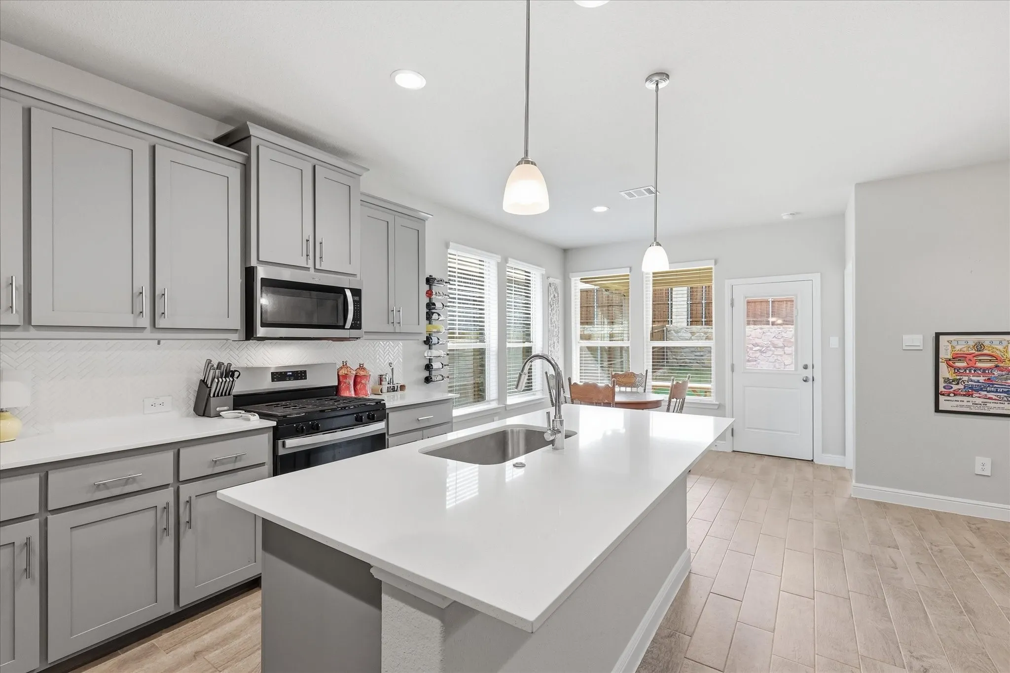 Kitchen featuring an island with a sink, stainless steel appliances, light gray cabinetry, white countertops, and wood-finish flooring