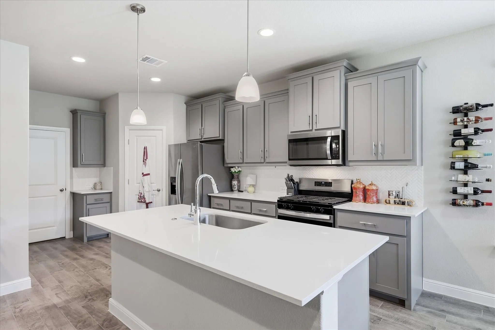 Kitchen featuring an island with an undermount sink, stainless steel appliances, grey cabinetry, a white backsplash, and wood-finish flooring