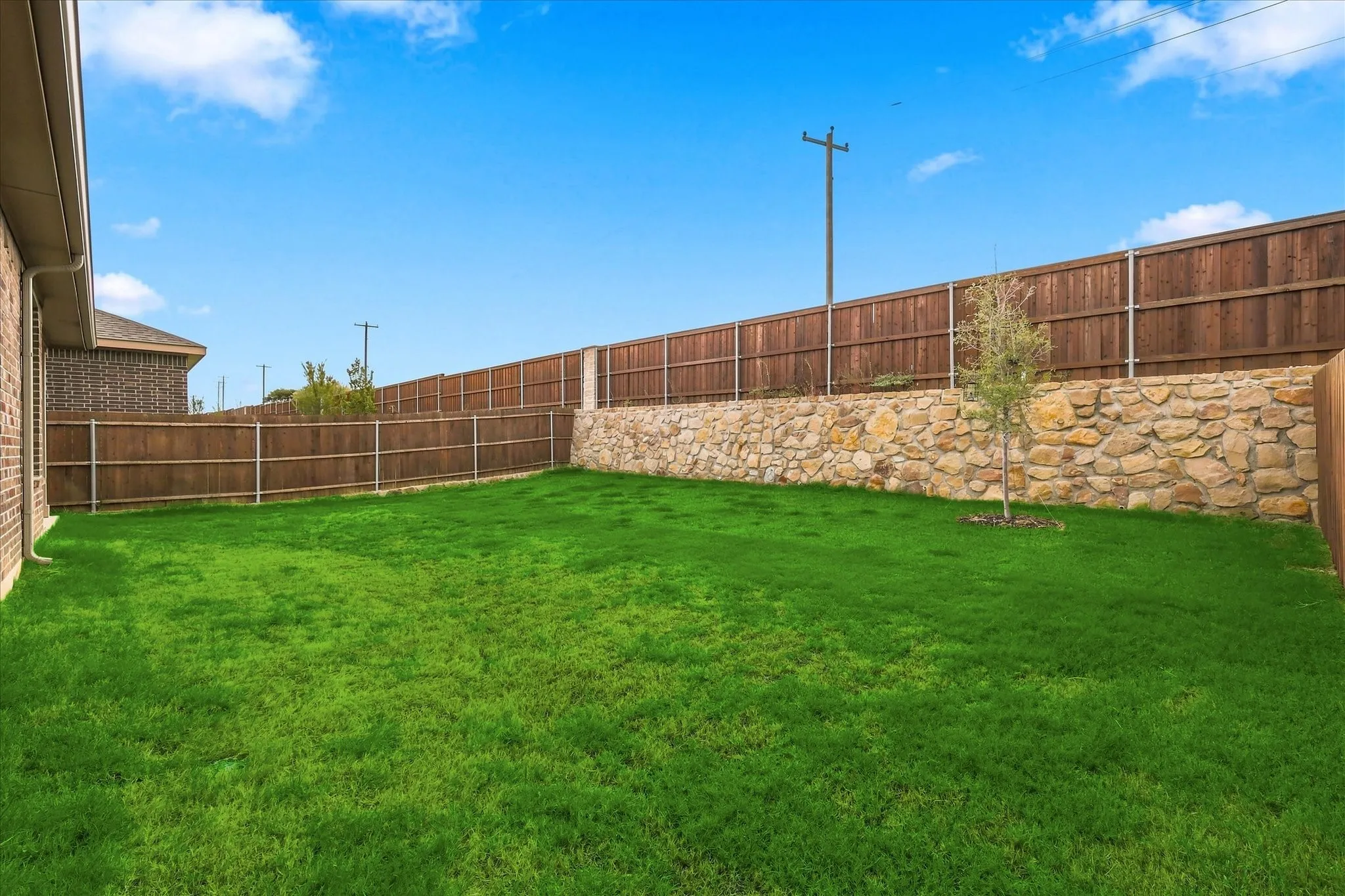 Expansive backyard featuring a manicured lawn, a stone retaining wall, and a full privacy fence