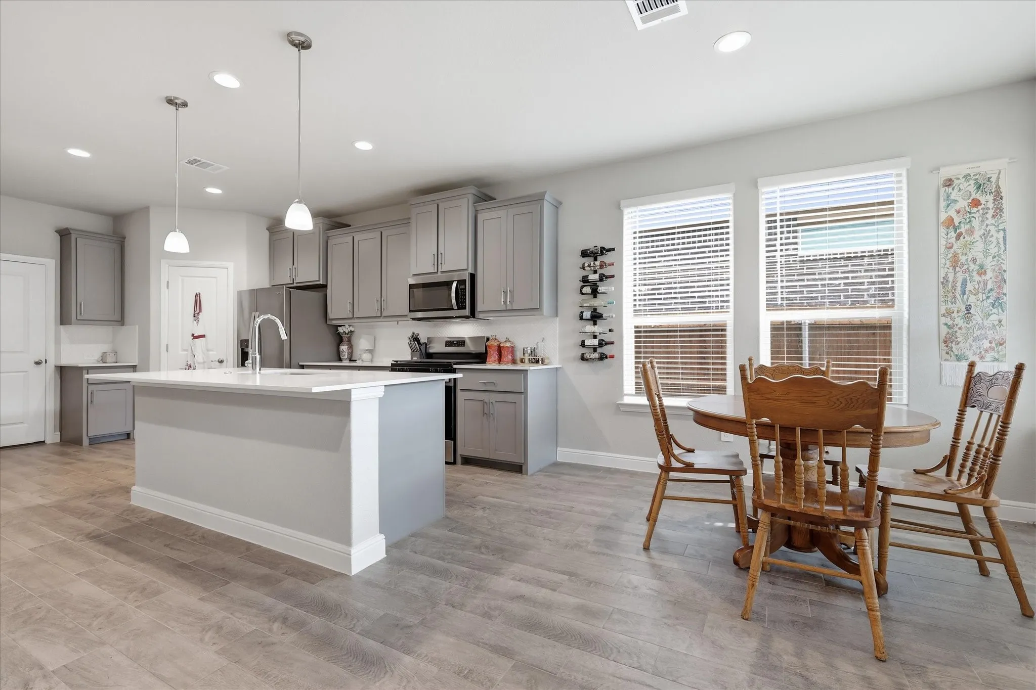 Open-concept kitchen and dining area featuring gray cabinetry, a central island with a sink, stainless steel appliances, and wood-finish flooring
