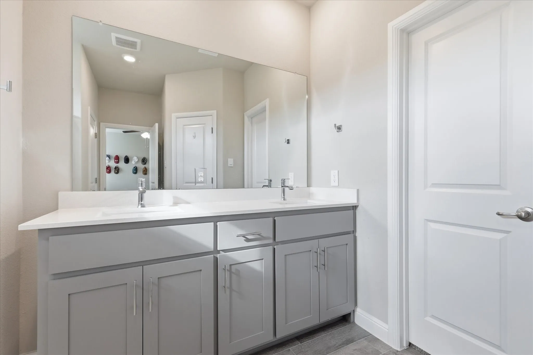 Dual sink vanity with light gray cabinetry, chrome hardware, white countertop, and expansive mirror