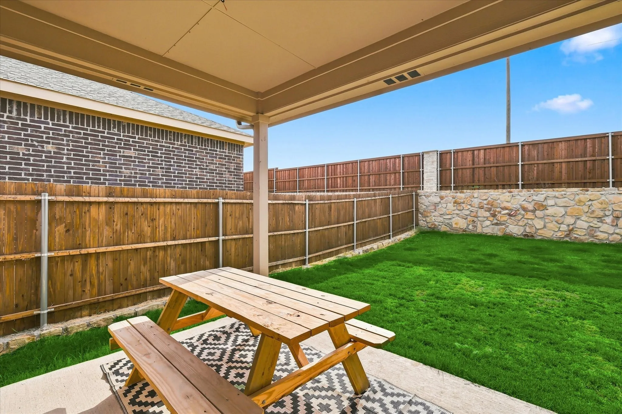 Covered patio with concrete flooring, private wood fencing, stone retaining wall, and an expansive lawn area