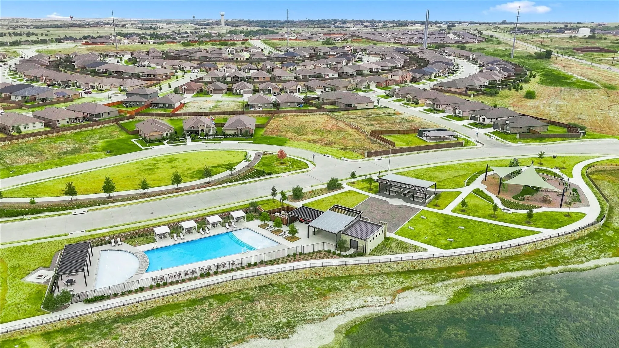 Community pool with integrated sun shelf, an adjacent covered lounge area, and a separate recreational park with shade structures