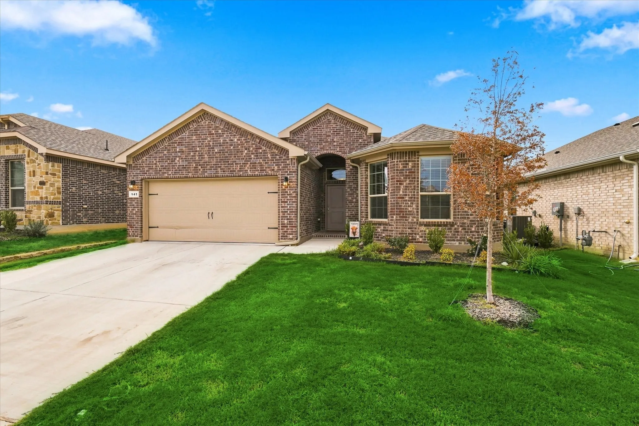 Brick exterior, two-car garage, concrete driveway, landscaped front yard, and a mature tree