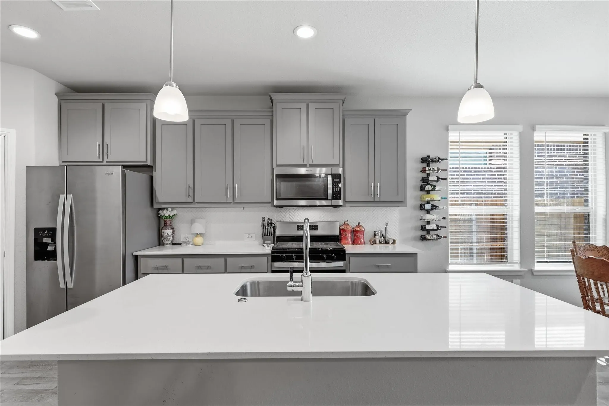 Kitchen featuring a large island with an undermount sink, pendant lighting, stainless steel appliances, and grey cabinetry
