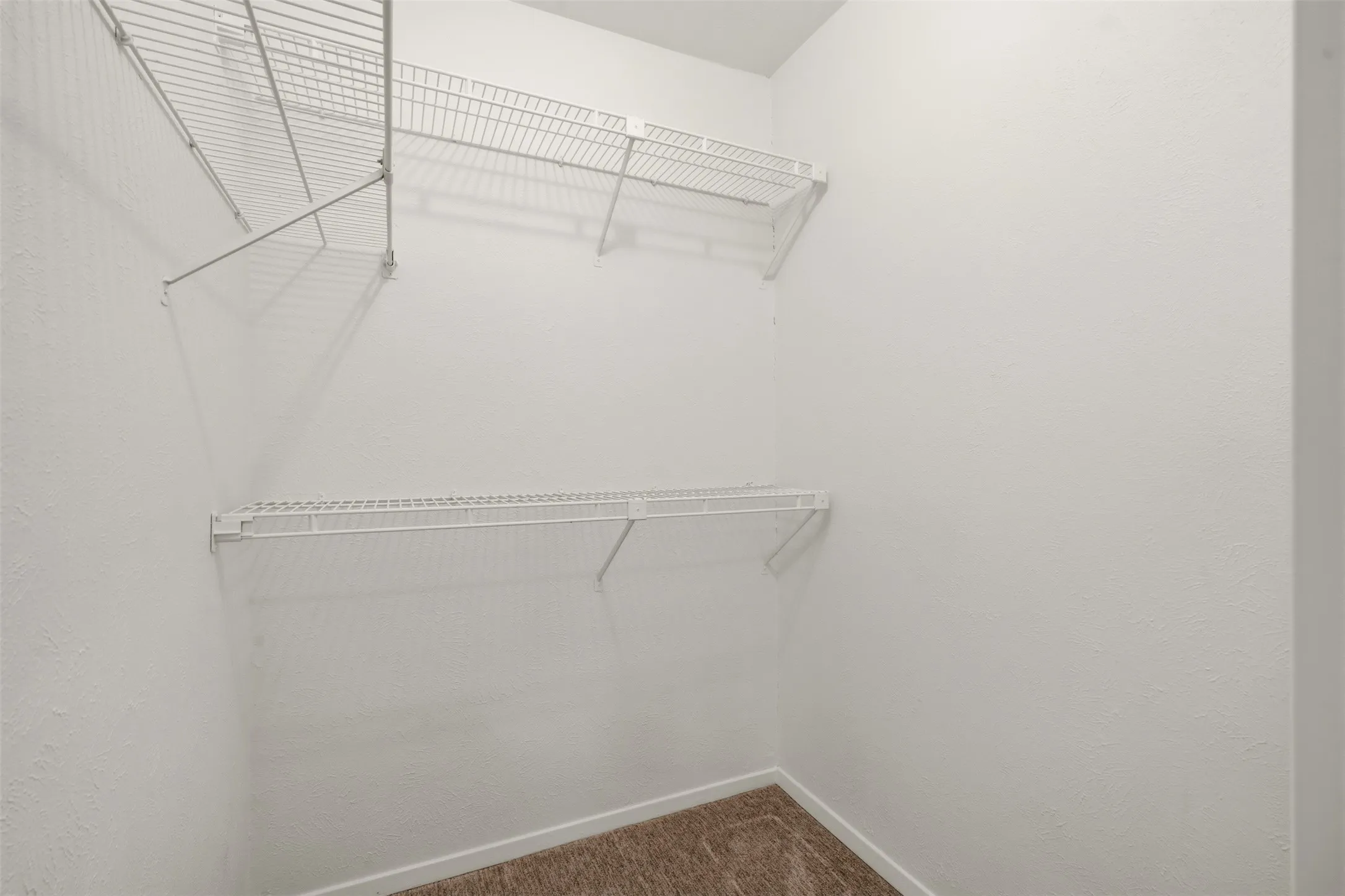 White wire shelving system with multiple tiers, textured white walls, and carpeting