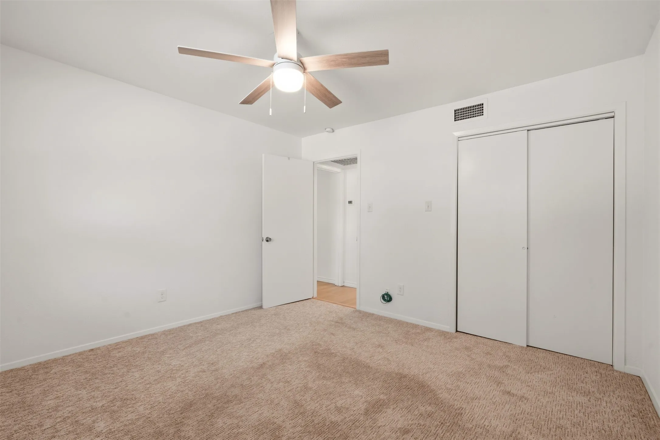 Carpeted flooring with a ceiling fan light fixture and sliding closet doors