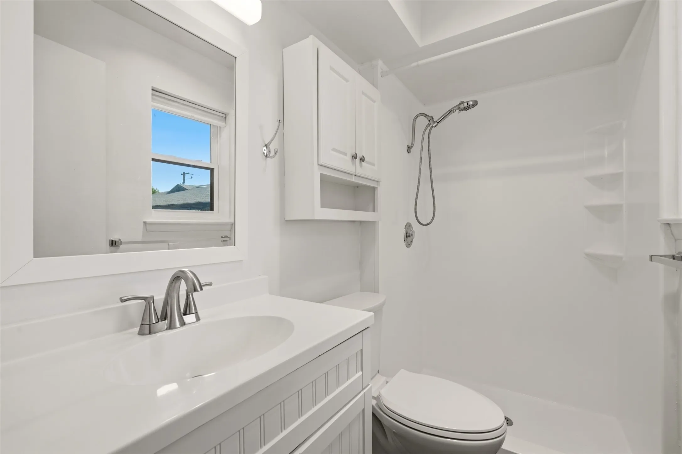 Spa-inspired bathroom featuring a floating vanity with quartz countertop and chrome faucet, white subway tile surround, frameless glass-enclosed shower with rainfall showerhead, toilet with elongated bowl, recessed medicine cabinet, and natural light from a picture window