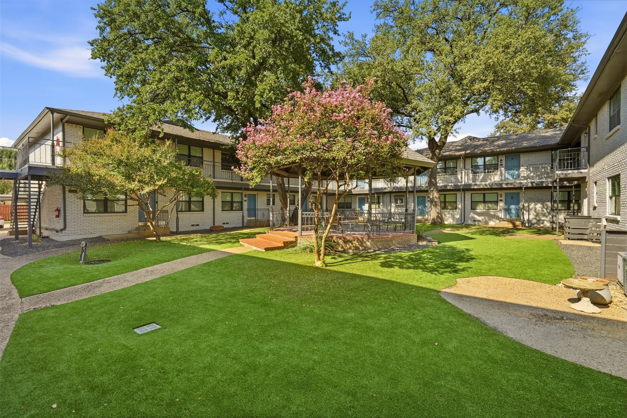 Central courtyard featuring manicured lawn, paved pathways, and a built-in gazebo with a raised platform
