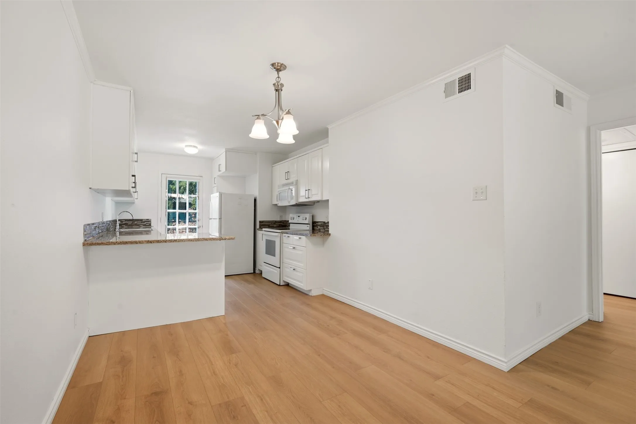 Kitchen featuring white cabinetry, light granite-style countertops, wood-finish flooring, a mosaic tile backsplash, and a white appliance package