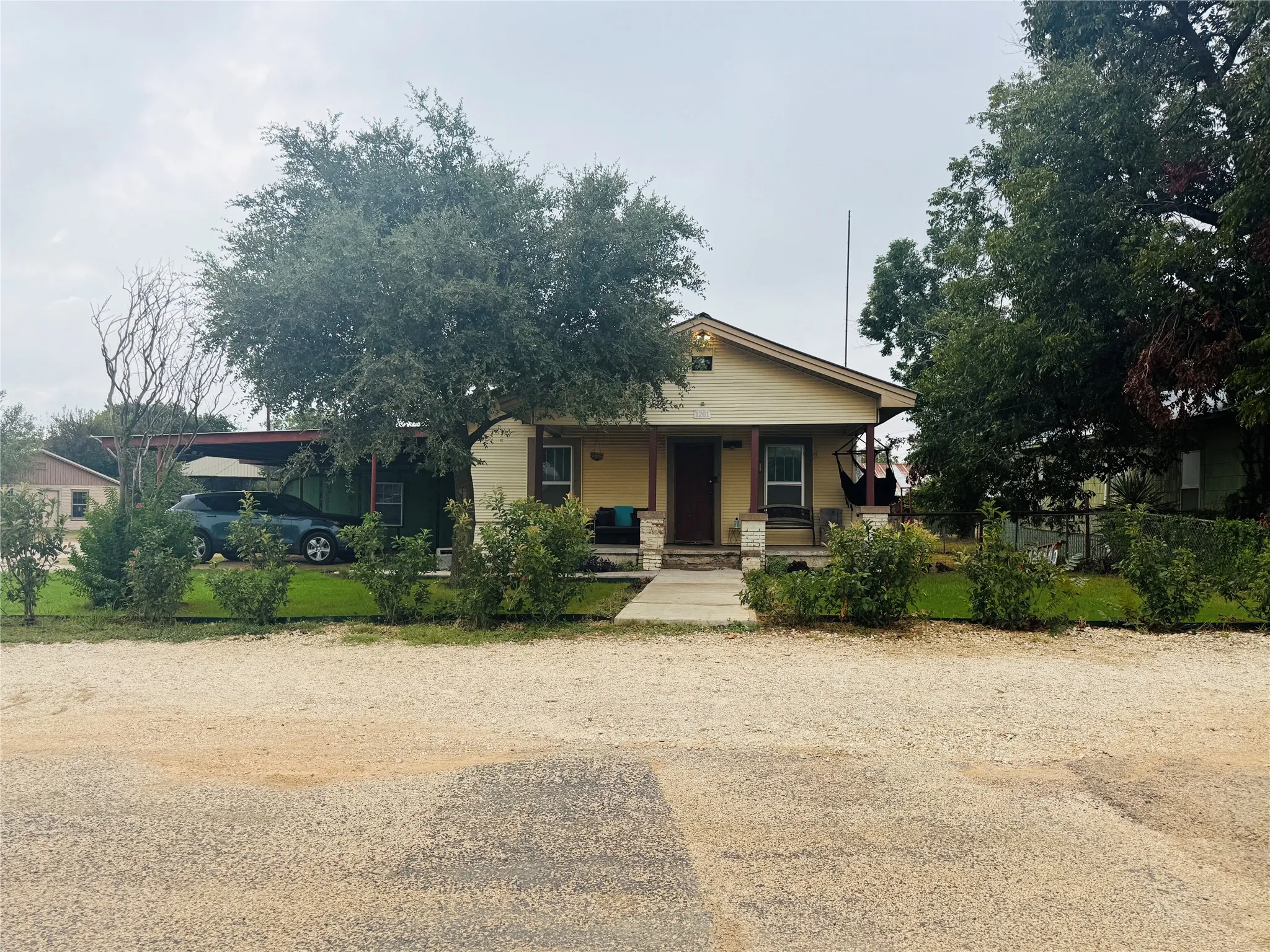 Single-story residence with a covered front porch featuring stone accents, a covered side carport, and mature trees on the property