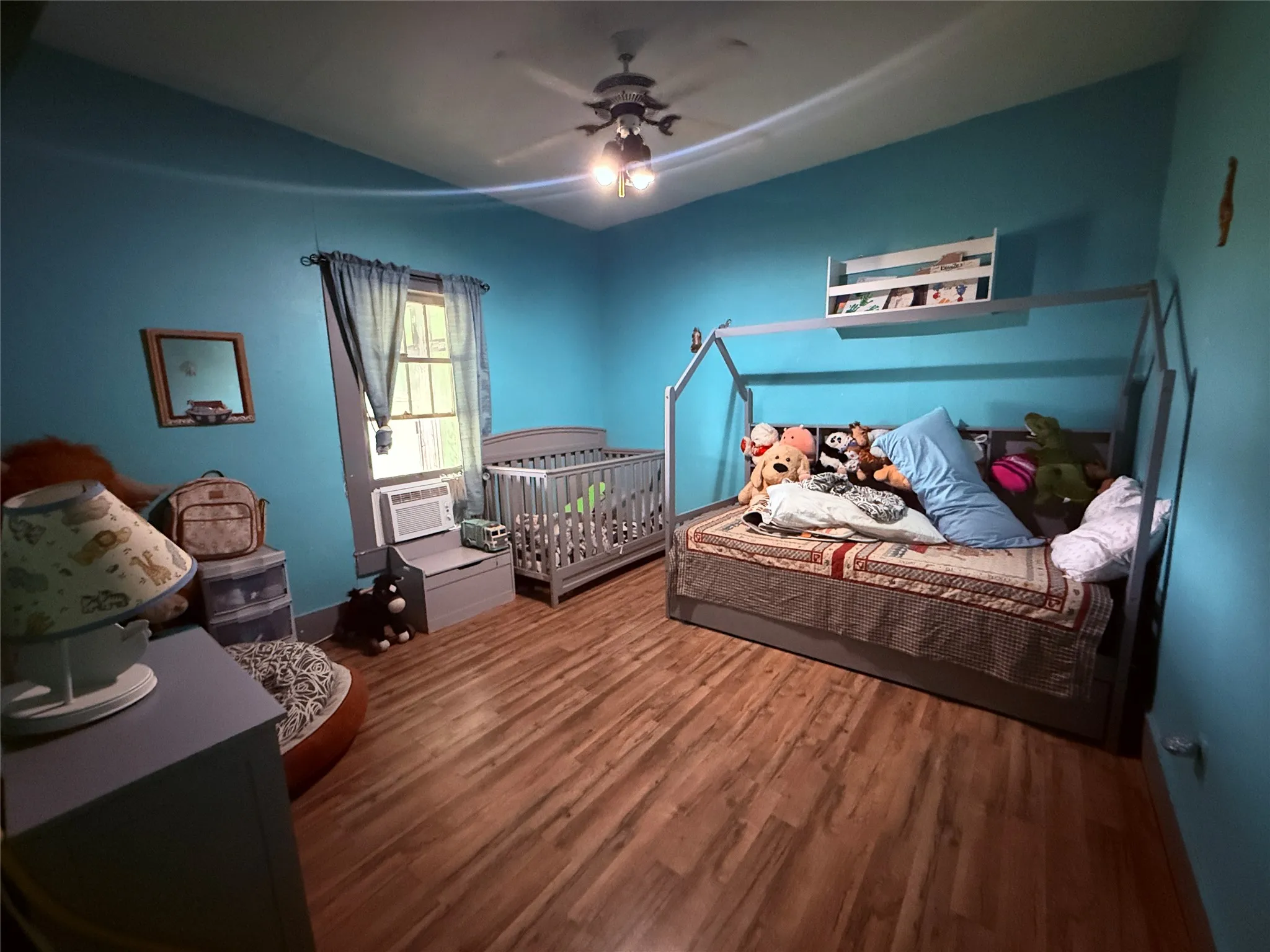 Wood-finish flooring, ceiling fan, window with trim, and a window-mounted air conditioning unit