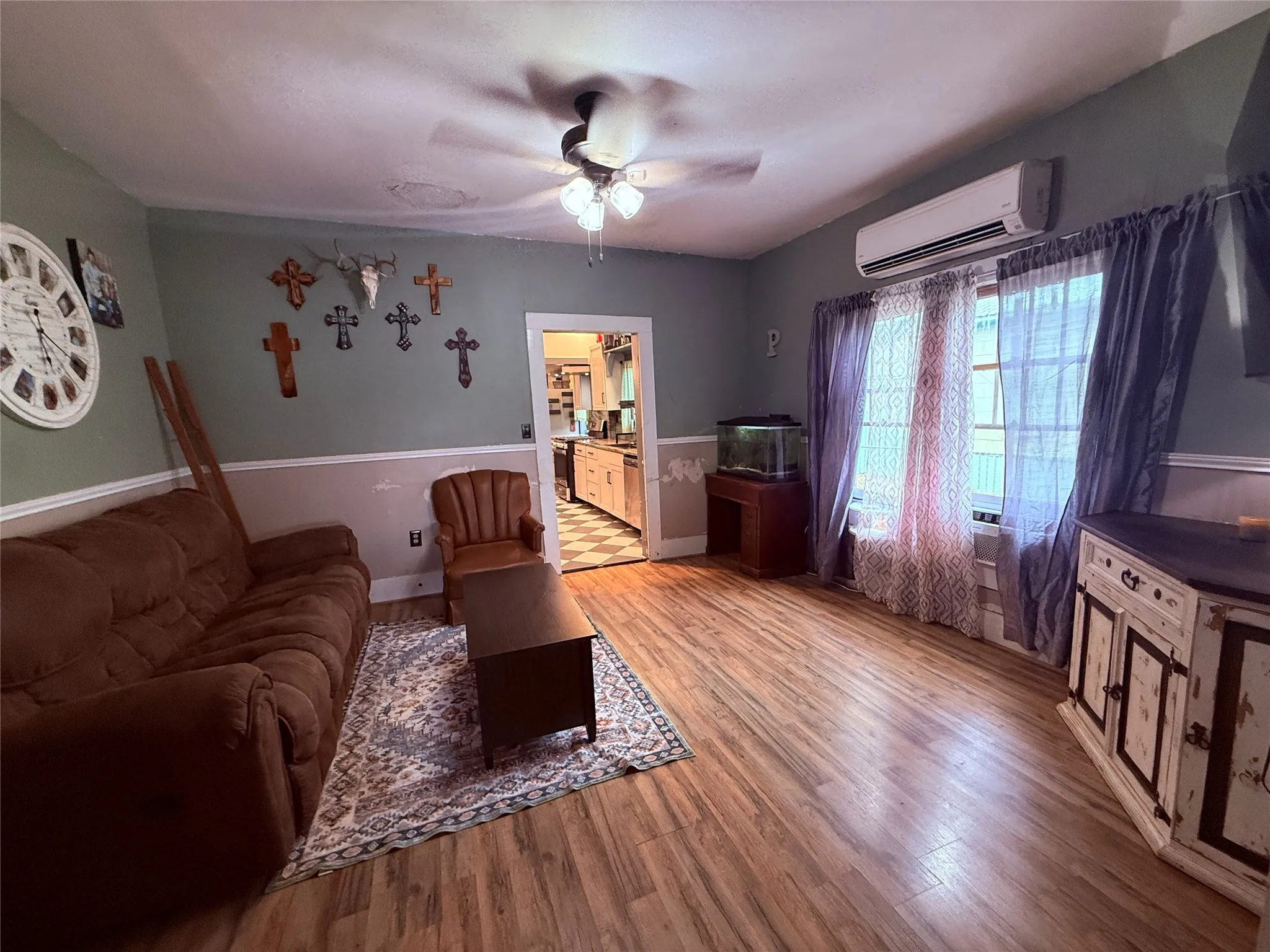 Wood-finish flooring throughout, ceiling fan with light fixture, and window with installed air conditioning unit