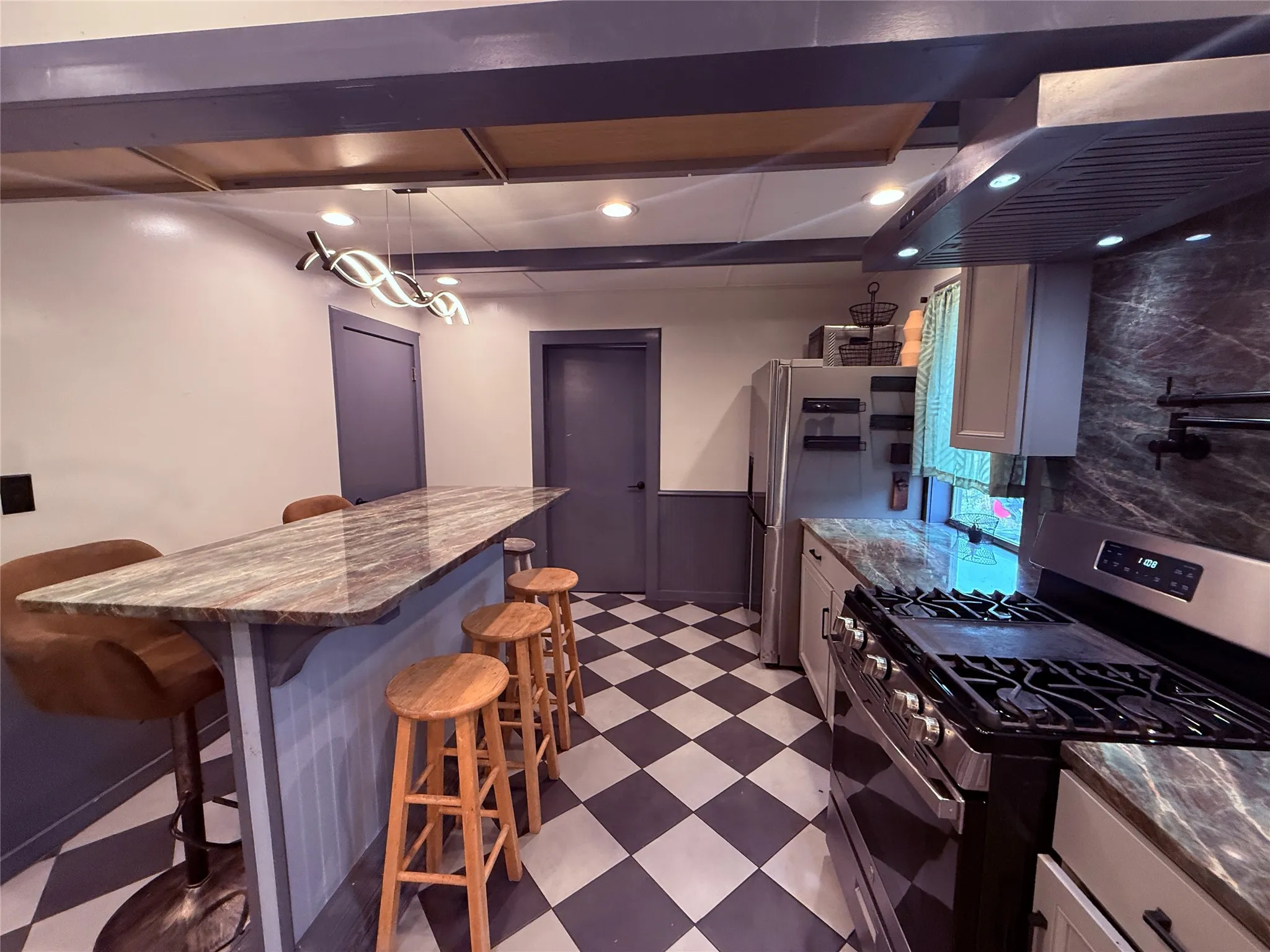 Kitchen featuring a checkerboard floor, built-in breakfast bar with a stone-finish countertop, stainless steel appliances, and recessed lighting