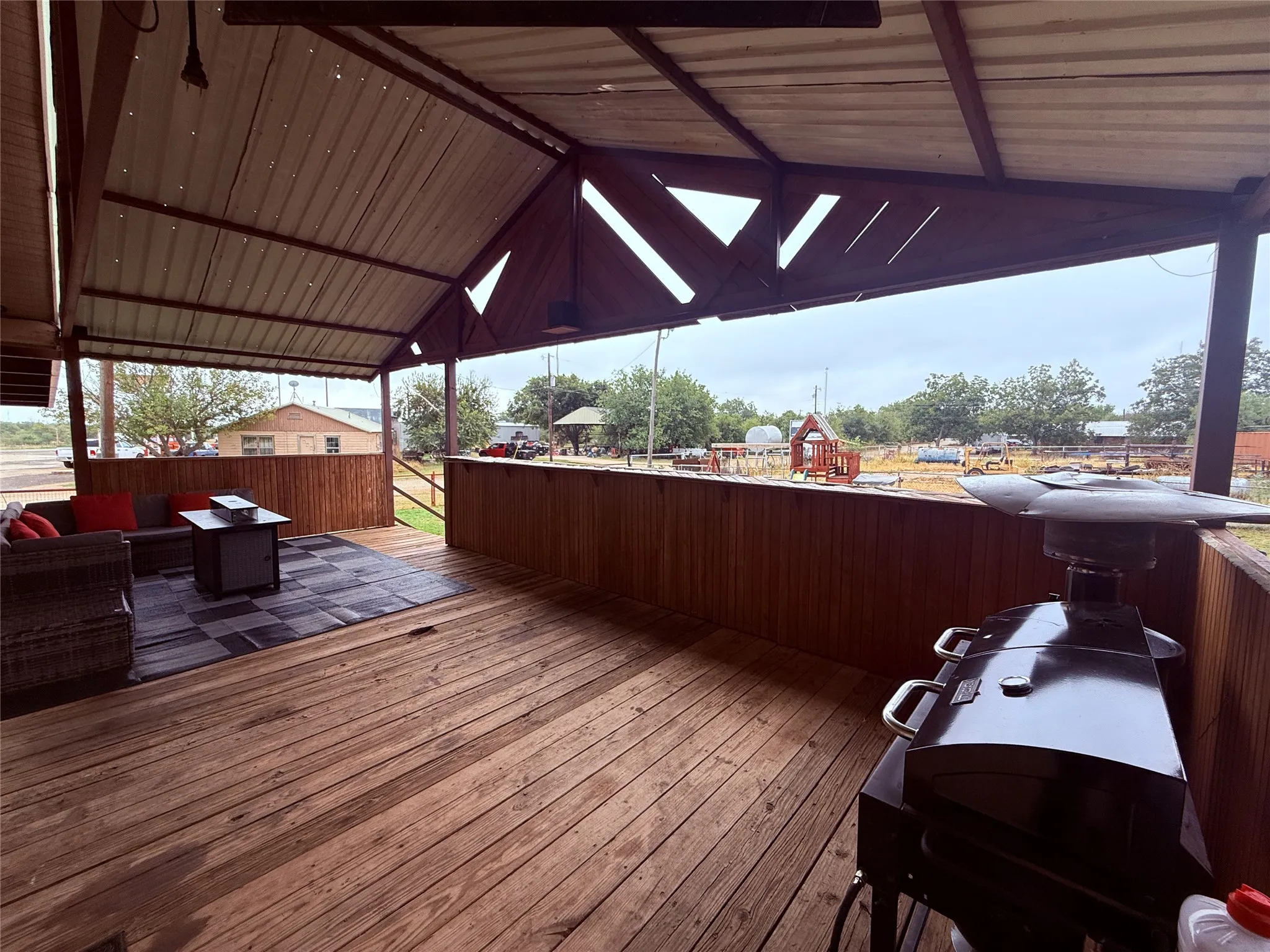 Expansive wood-finish deck with a built-in privacy wall, covered by a pitched metal roof, featuring exposed wood beams