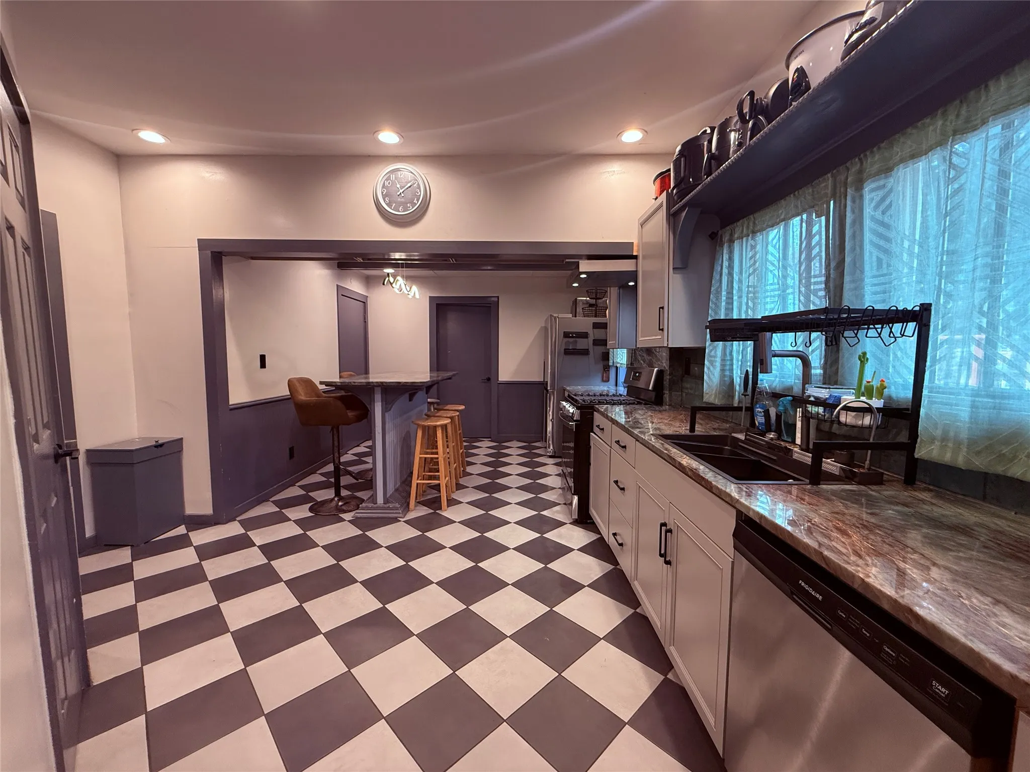 Kitchen featuring checkered flooring, light gray cabinetry, a built-in dishwasher, an undermount sink, and a high-top counter