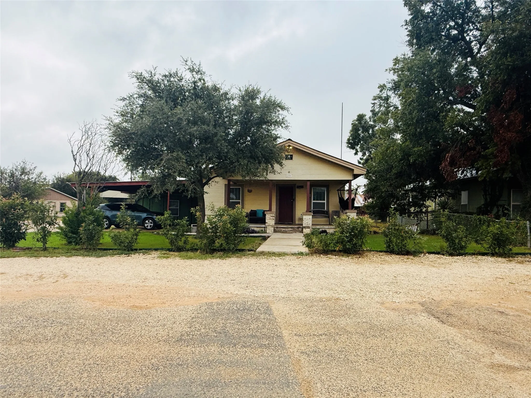 Exterior featuring a covered front porch, carport, and mature trees