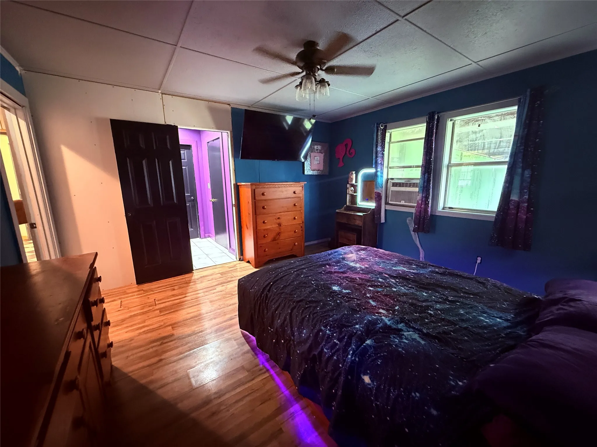 Wood-finish flooring, two large windows, ceiling fan with integrated lighting, and a paneled door